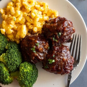 Close up of BBQ meatballs on a cream plate with mac and cheese and steamed broccoli.