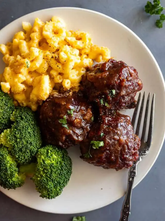 Close up of BBQ meatballs on a cream plate with mac and cheese and steamed broccoli.