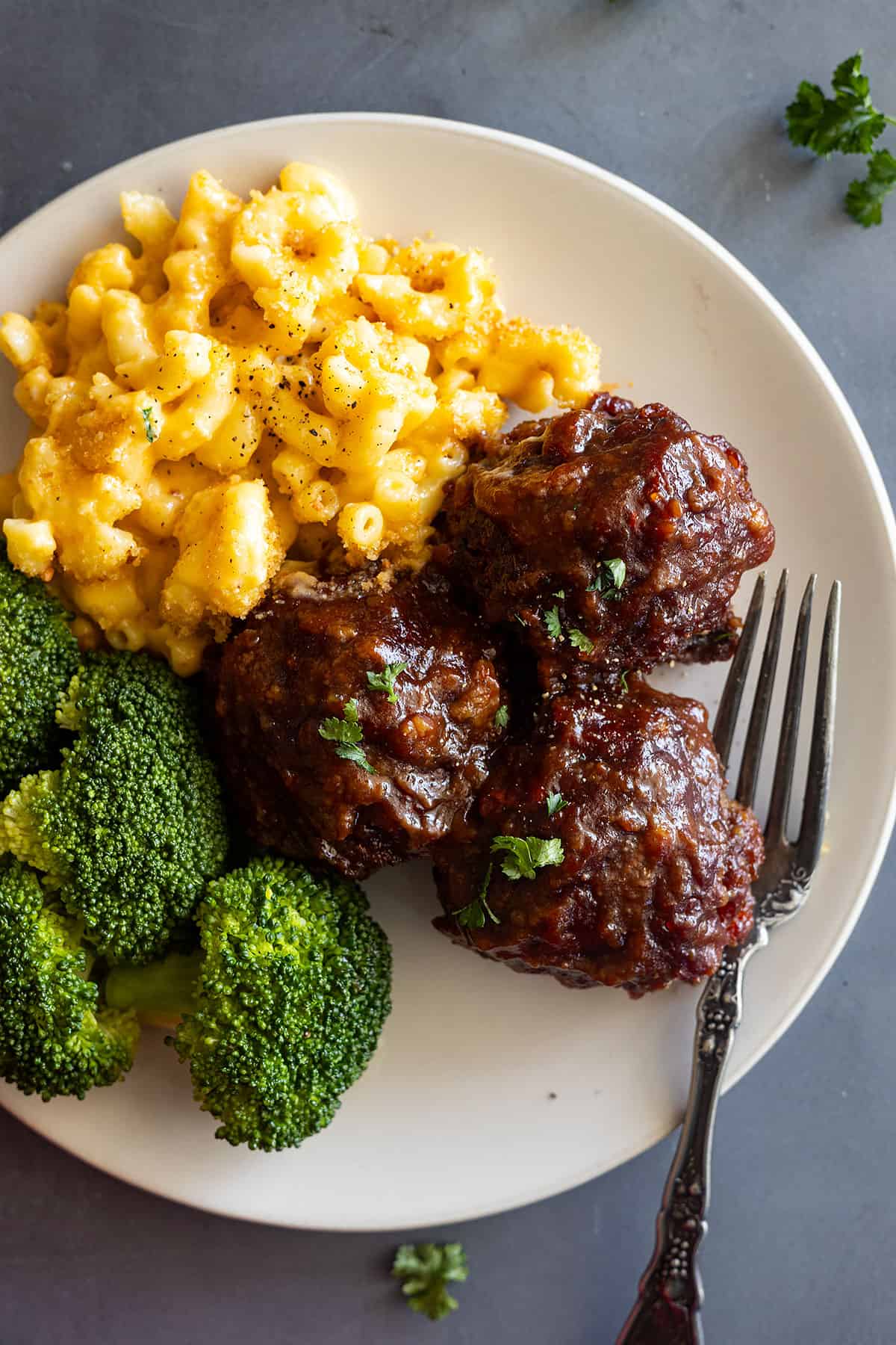 Close up of BBQ meatballs on a cream plate with mac and cheese and steamed broccoli.