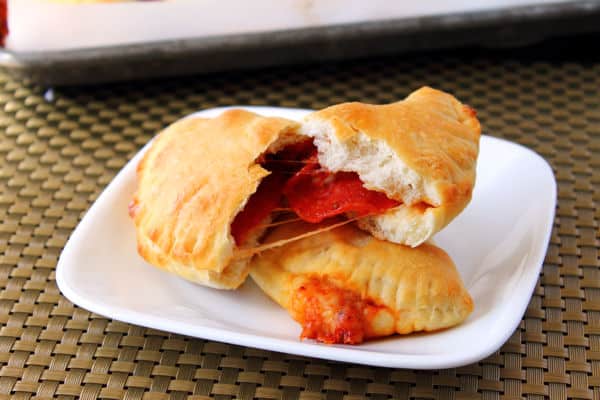 Pepperoni Pizza pockets on a plate with one torn open so you can see the pizza sauce and cheese inside