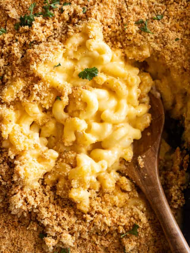 Overhead view of homemade mac and cheese in a casserole dish fresh from the oven. Wooden spoon dipping into the dish.