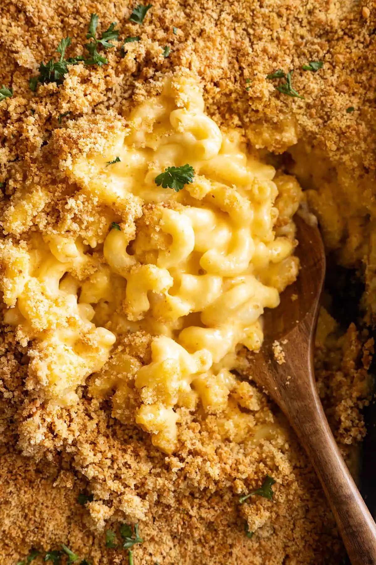 Overhead view of homemade mac and cheese in a casserole dish fresh from the oven. Wooden spoon dipping into the dish. 