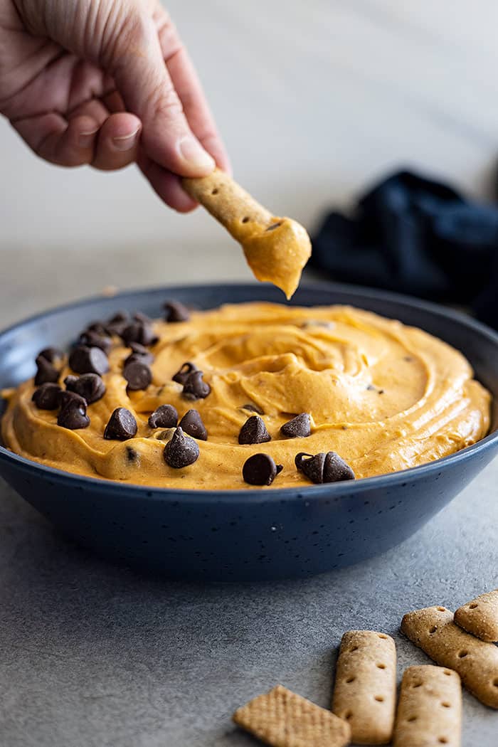 A hand holding a graham cracker stick dipping into the dip. 