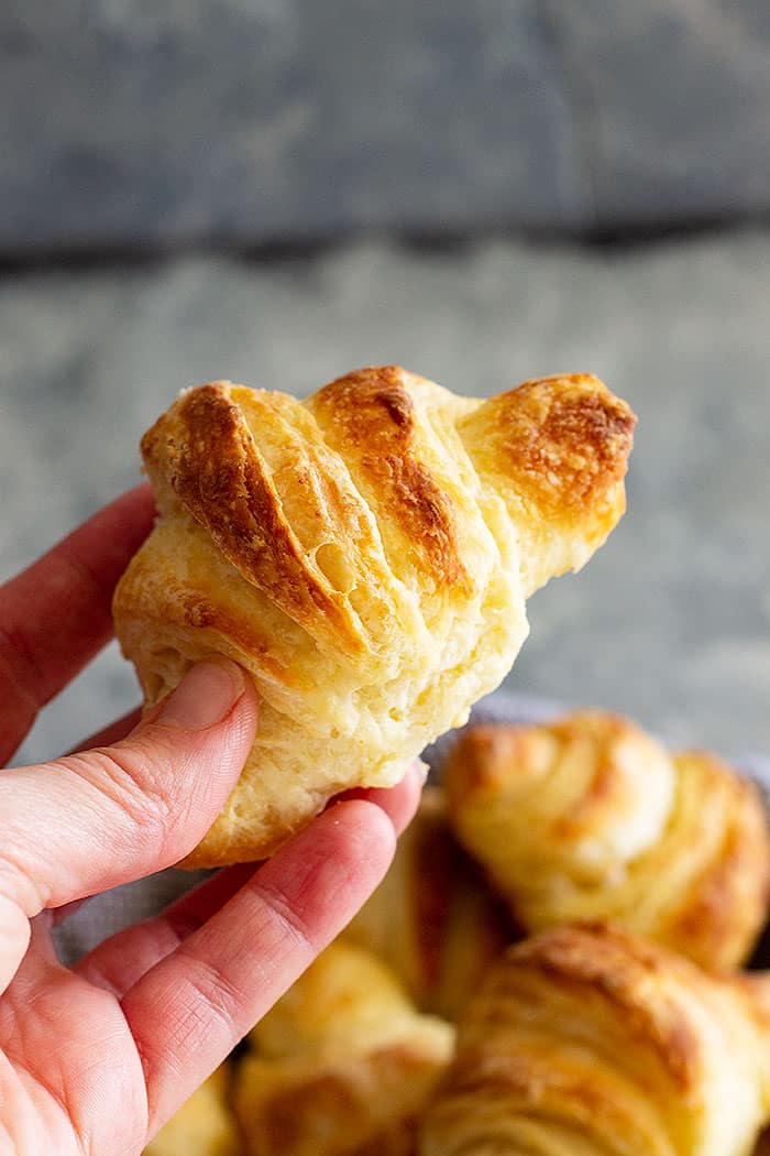 A hand holding up a flaky crescent roll. 