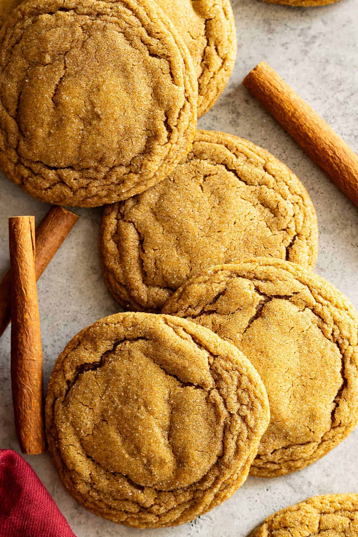 Overhead view of molasses cookies scattered. Cinnamon sticks off to the sides.