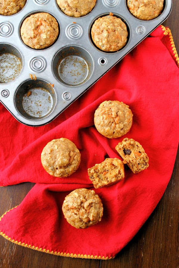 healthy breakfast muffins with banana, oatmeal, and raisins both in a muffin tray and on a red cloth beside the try