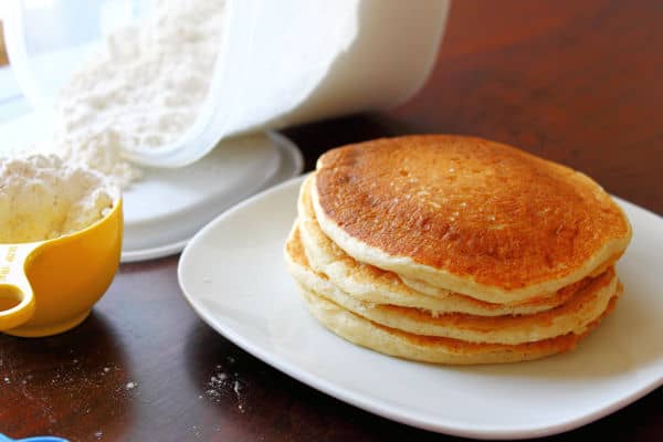 a stack of fluffy homemade pancakes with mix in the background