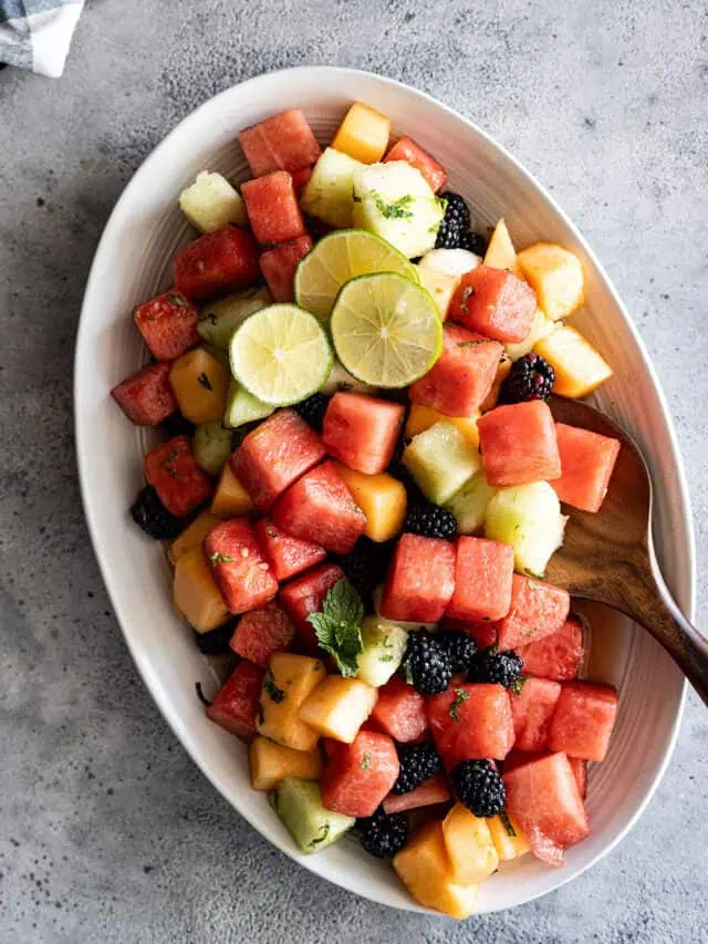 Overhead view of salad on a serving plate garnished with lime slices and mint.