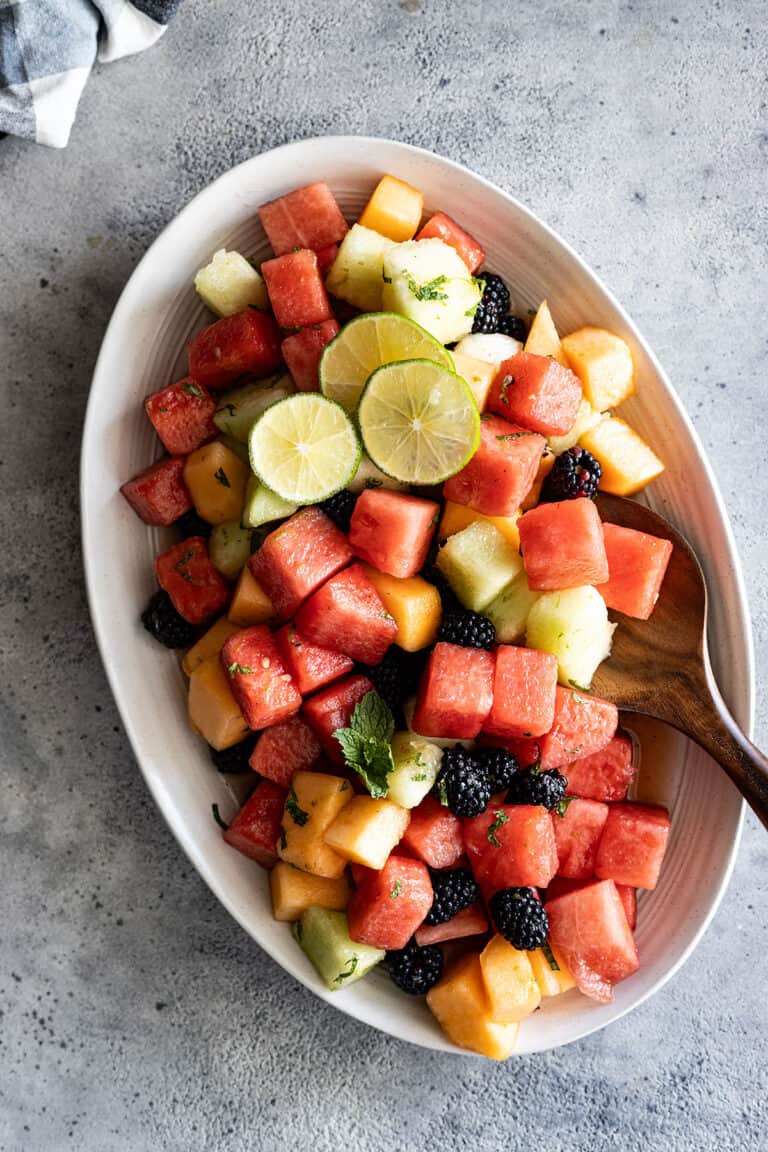 Overhead view of salad on a serving plate garnished with lime slices and mint.
