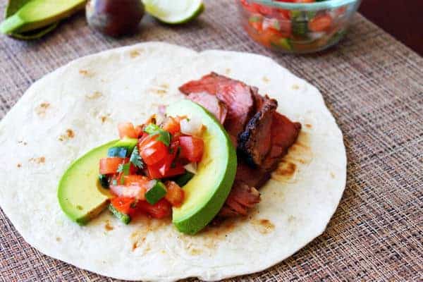 slices of grilled steak in a taco shell with slices of avocado and a spoonful of pico de gallo