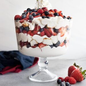 A trifle bowl filled with angel food cake, coconut cheesecake filling, strawberries, blueberries, and raspberries. All in pretty layers.