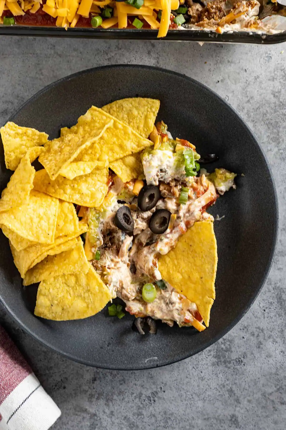 Overhead picture of taco dip on a plate with chips surrounding it. 