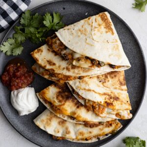 Overhead view of quesadillas on a dark plate with sour cream and salsa off to the side.