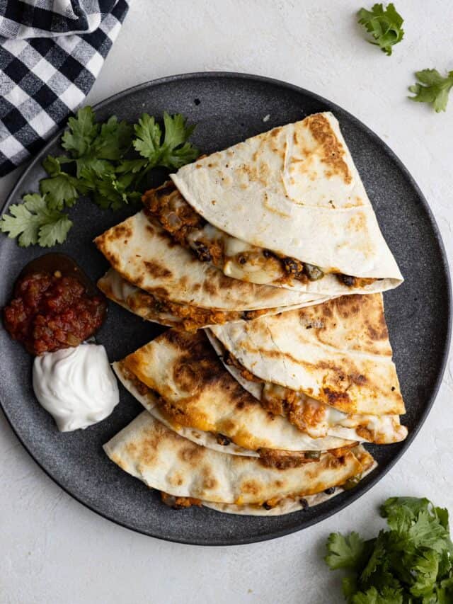 Overhead view of quesadillas on a dark plate with sour cream and salsa off to the side.
