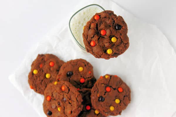a group of Double Chocolate Peanut Butter Cookies in the background with a single cookie on the rim of a glass of milk