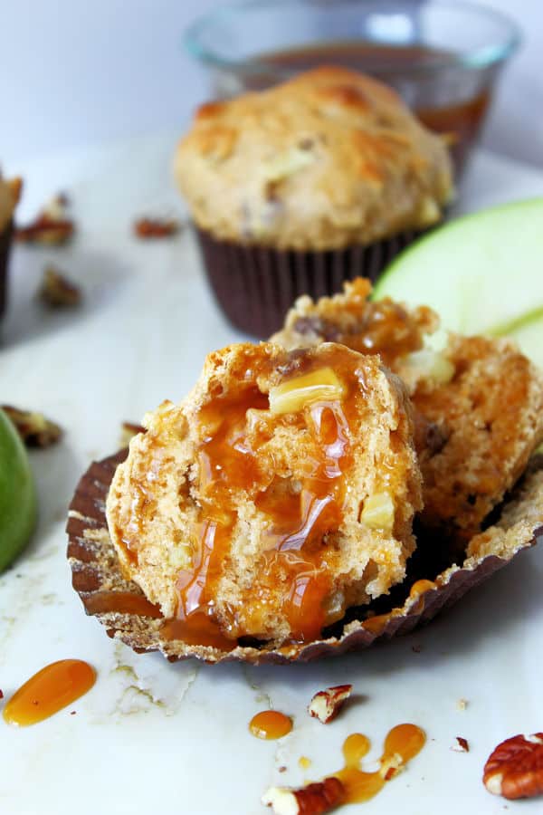 apple muffin baked with pecans cut open inside its muffin tin with caramel drizzled on top