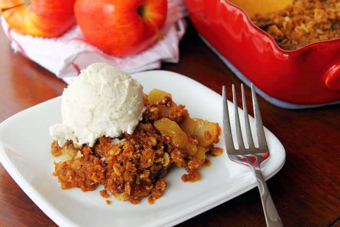 a fork leaning on a white plate that contains a serving of apple crisp with a scoop of vanilla ice cream on top