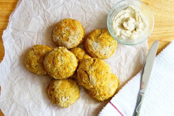 overhead shot of pumpkin biscuits arranged on parchment paper with a glass bowl of maple butter and a knit beside them