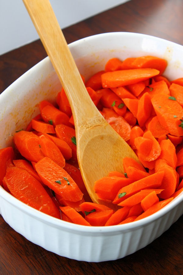 ginger maple glazed carrots in a white serving dish with a wooden spoon 