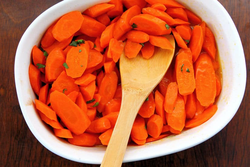 overhead photo of maple glazed carrots in a white serving bowl with a wooden spoon 