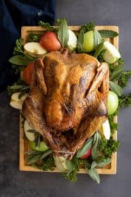 Overhead view of Herb Roasted Turkey on a cutting board garnished with apples and herbs.