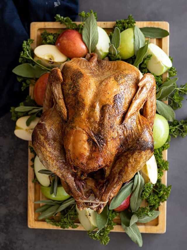 Overhead view of Herb Roasted Turkey on a cutting board garnished with apples and herbs.