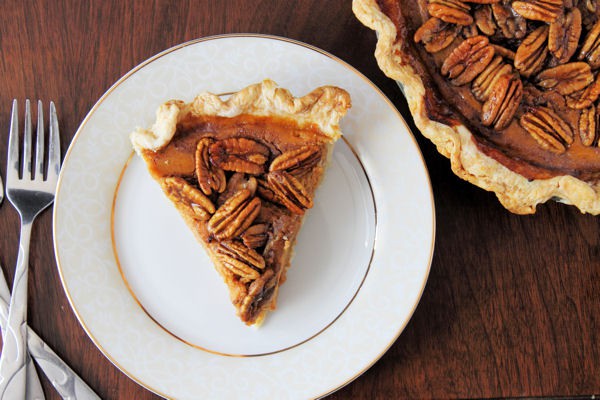 an overhead shot of a slice of Pumpkin Pie with Candied Pecans on a nice dinner plate with the rest of the pie in the right corner