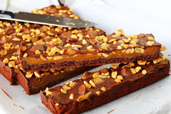 layered Peanut Butter and Caramel Brownies cut into slices with nut topping