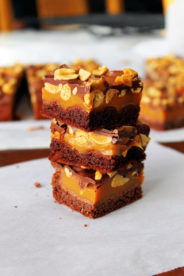 three peanut butter caramel brownies cut into squares and stacked on top of each other