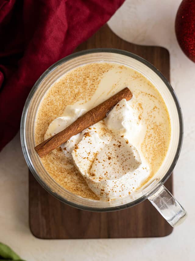 Overhead view of eggnog in a large cup topped with whipped cream and a cinnamon stick.