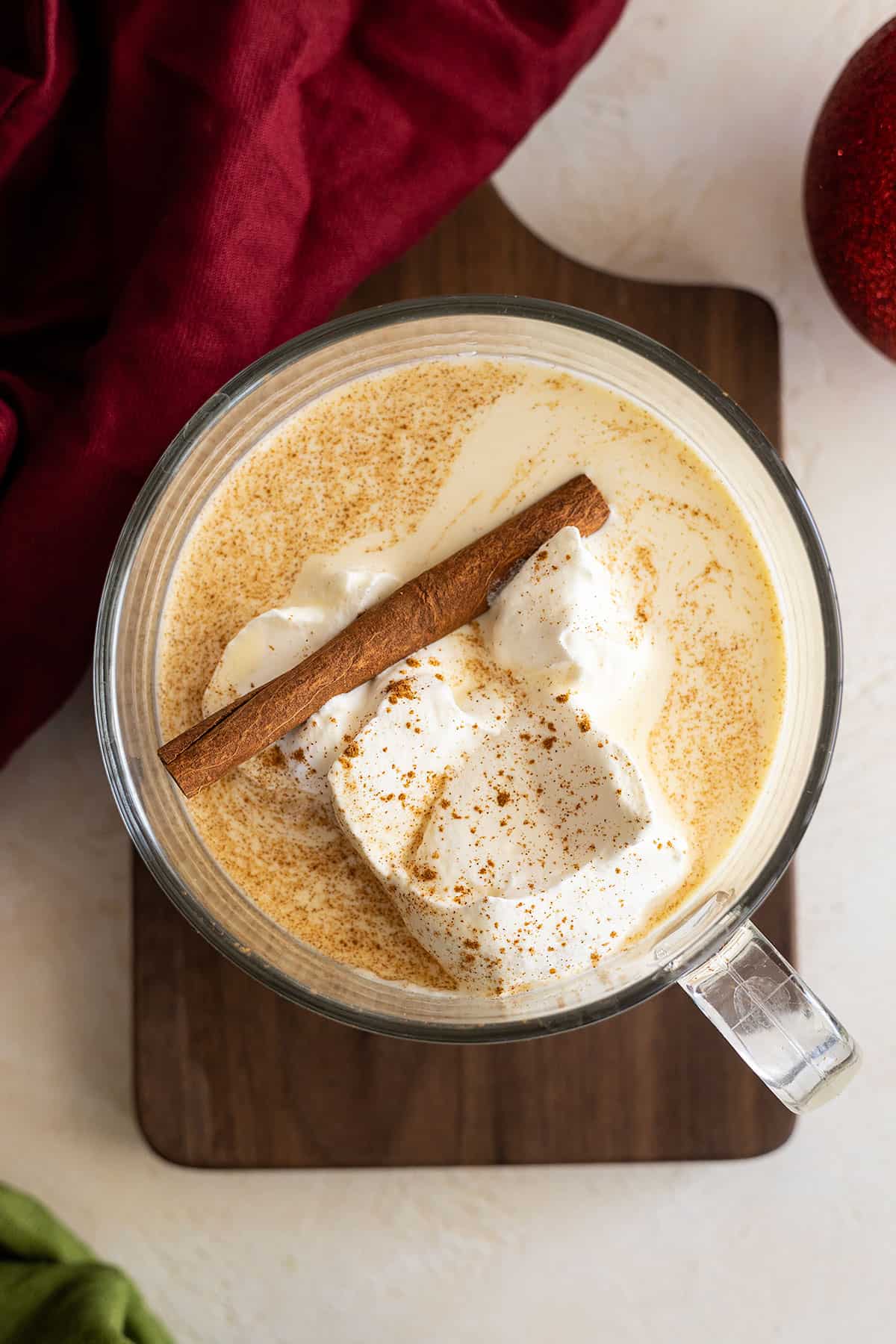Overhead view of eggnog in a large cup topped with whipped cream and a cinnamon stick. 