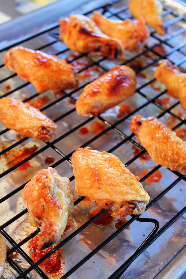 a foil lined baking sheet with a cooling rack on top of it and crispy baked wings placed on the rack so the juices and excess sauce will drip through onto the foil
