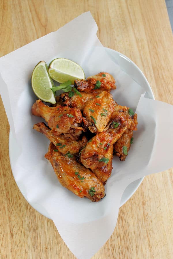 Crispy oven Baked Spicy Margarita Wing in a parchment paper lined white bowl alongside fresh lime and garnish on top