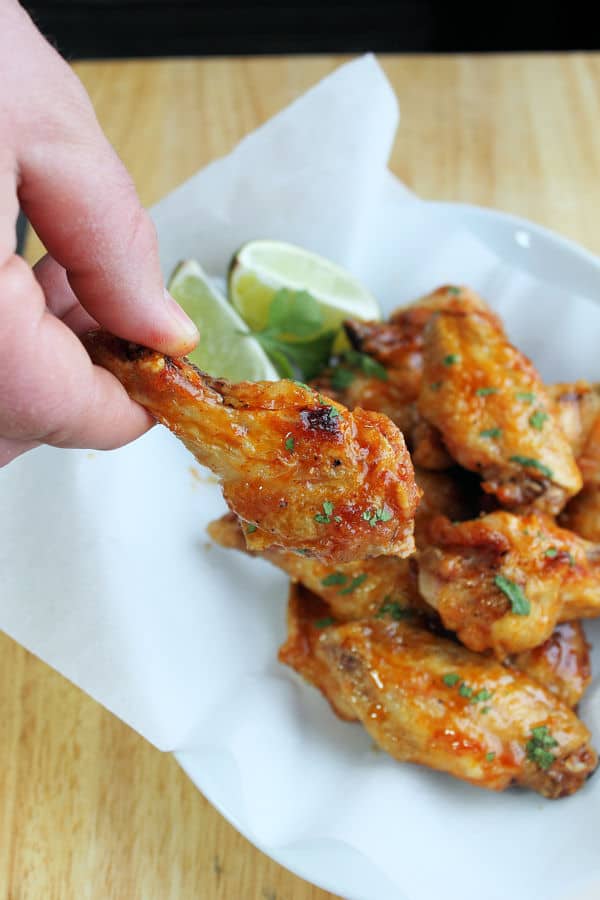 crispy oven baked wings coated in a spicy margarita sauce in a parchment line bowl in the background, but with one hand holding a single wing closer to the camera