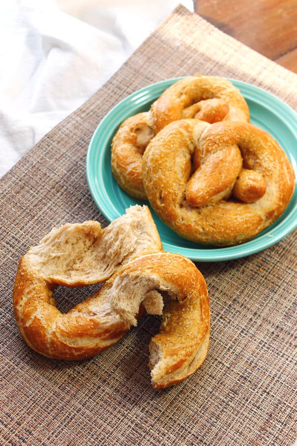 Homemade soft pretzels pictured with two on a teal green plate and one torn apart leaning against the plate
