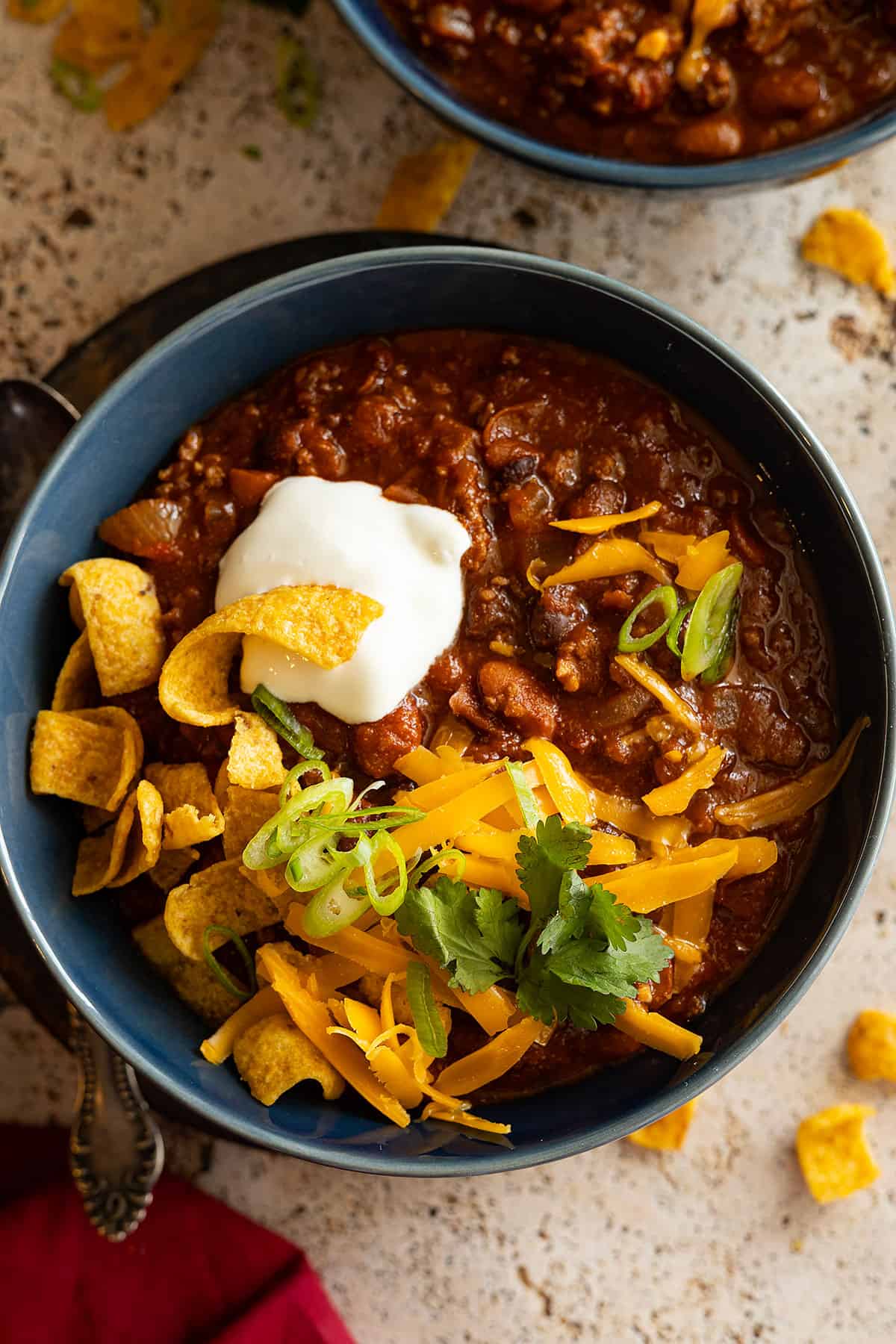 Overhead view of chili in a blue bowl topped with sour cream, cheese, and corn chips. 