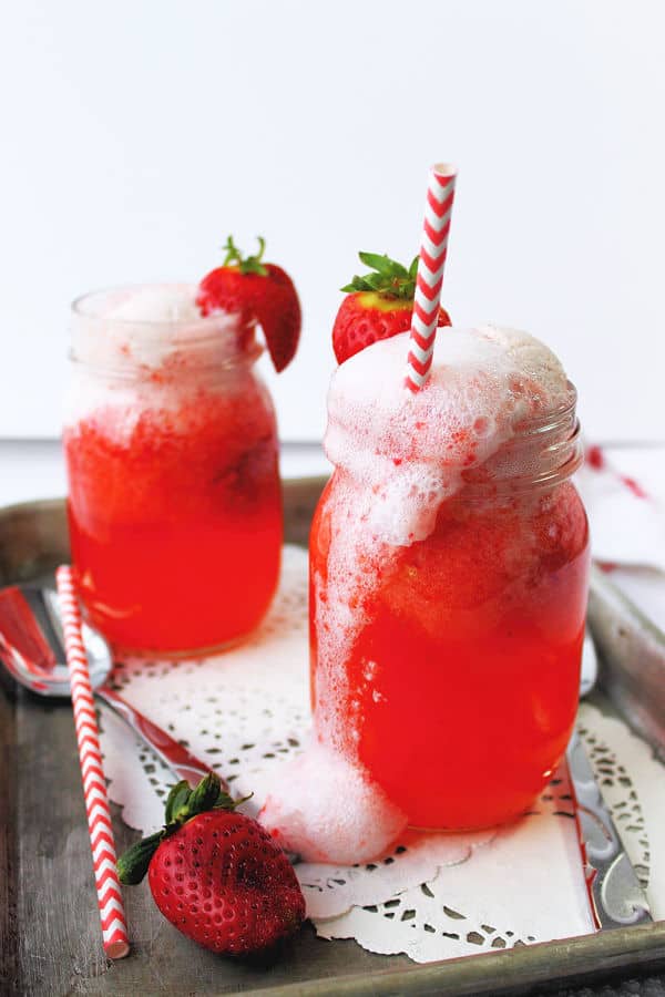 Strawberry floats in mason jars, topped with a fresh sliced strawberry, and a red and white straw. 