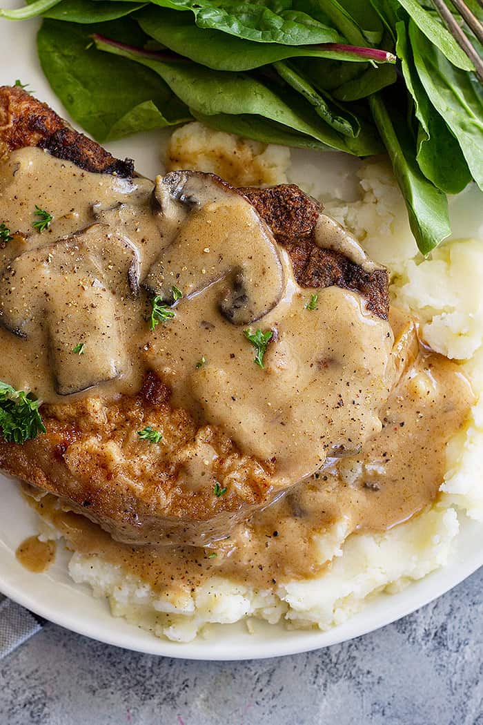 A pork chop plated on top of mashed potatoes and topped with a creamy mushroom sauce. 