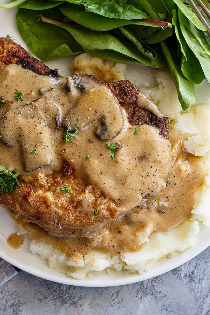 A pork chop plated on top of mashed potatoes and topped with a creamy mushroom sauce.