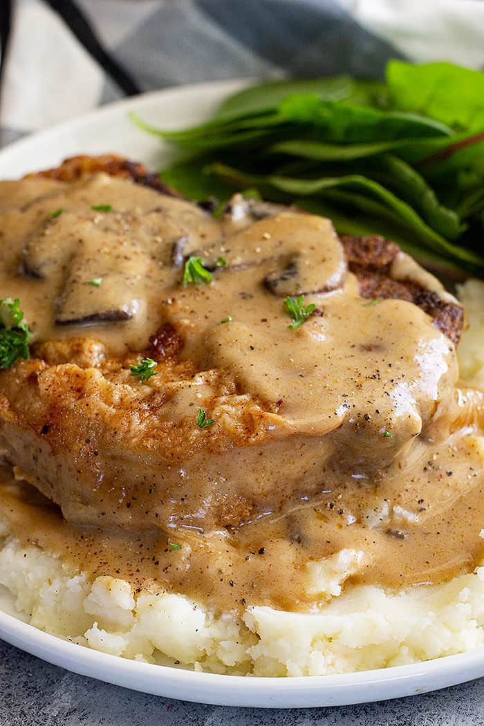 Close up of pork chop on a bed of mashed potatoes smothered in creamy mushroom gravy.