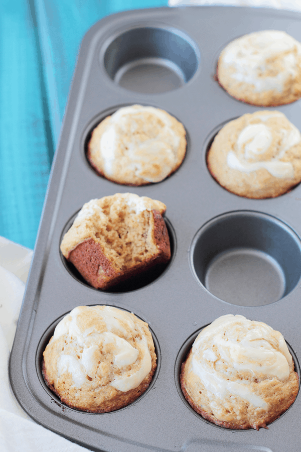 a muffin tin with banana muffins in them, some spots are empty and one muffin has a bite taken out of it 