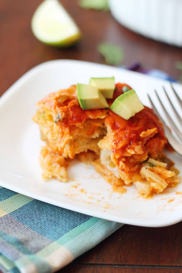 a serving of chicken enchilada bake on a white plate with avocado on top and a bite taken out of it 