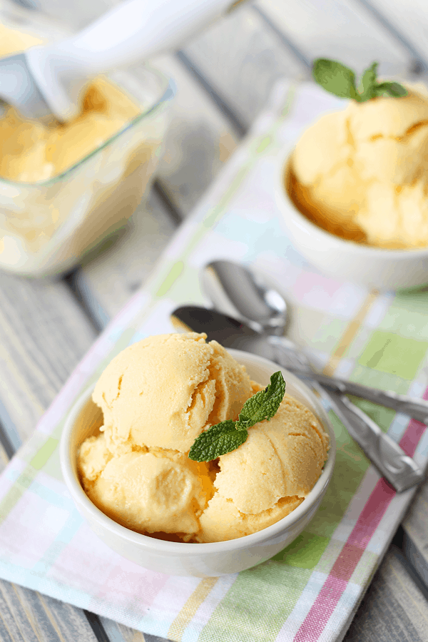 Mango frozen yogurt in circular white dish, topped with a sprig of fresh mint. 