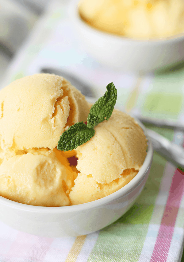 Mango frozen yogurt in circular white dish, topped with a sprig of fresh mint.