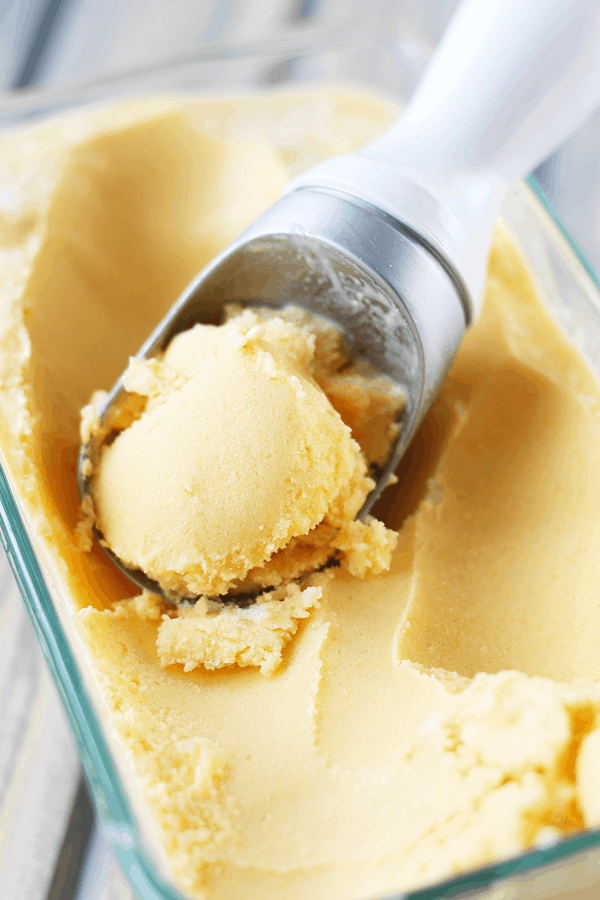 Frozen Mango Yogurt in freezer-safe container with a scoop in ice cream scoop. 