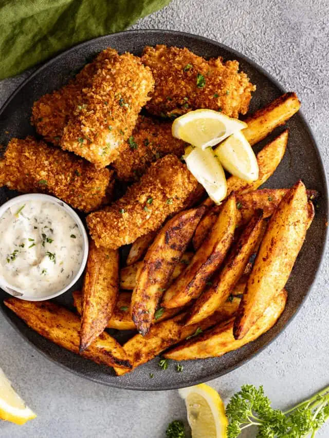 Overhead view of fish and chips on a plate garnished with lemon wedges. Tartar sauce off to the side.