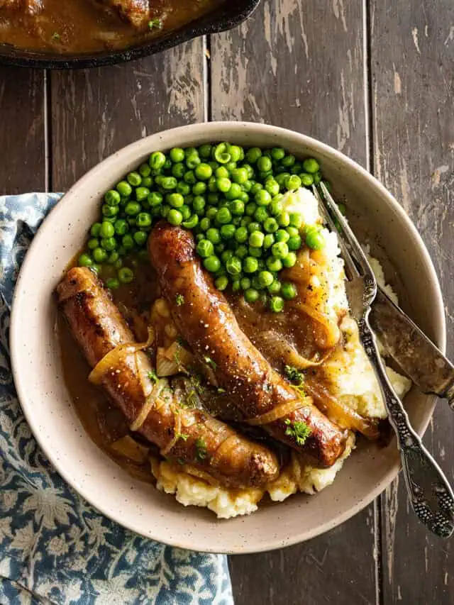Overhead picture of bangers and mash on a plate with peas on the side.