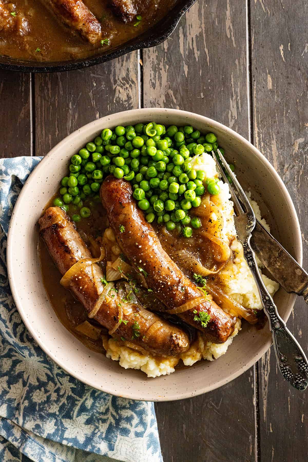 Overhead picture of bangers and mash on a plate with peas on the side.