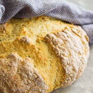 Round loaf of Traditional Irish Soda Bread wrapped in a towel.