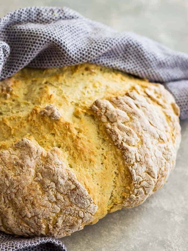 Round loaf of Traditional Irish Soda Bread wrapped in a towel.